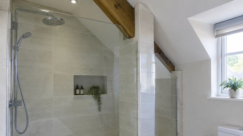 A shower screen panel notched around boxed pipework and a roof purlin in a loft bathroom